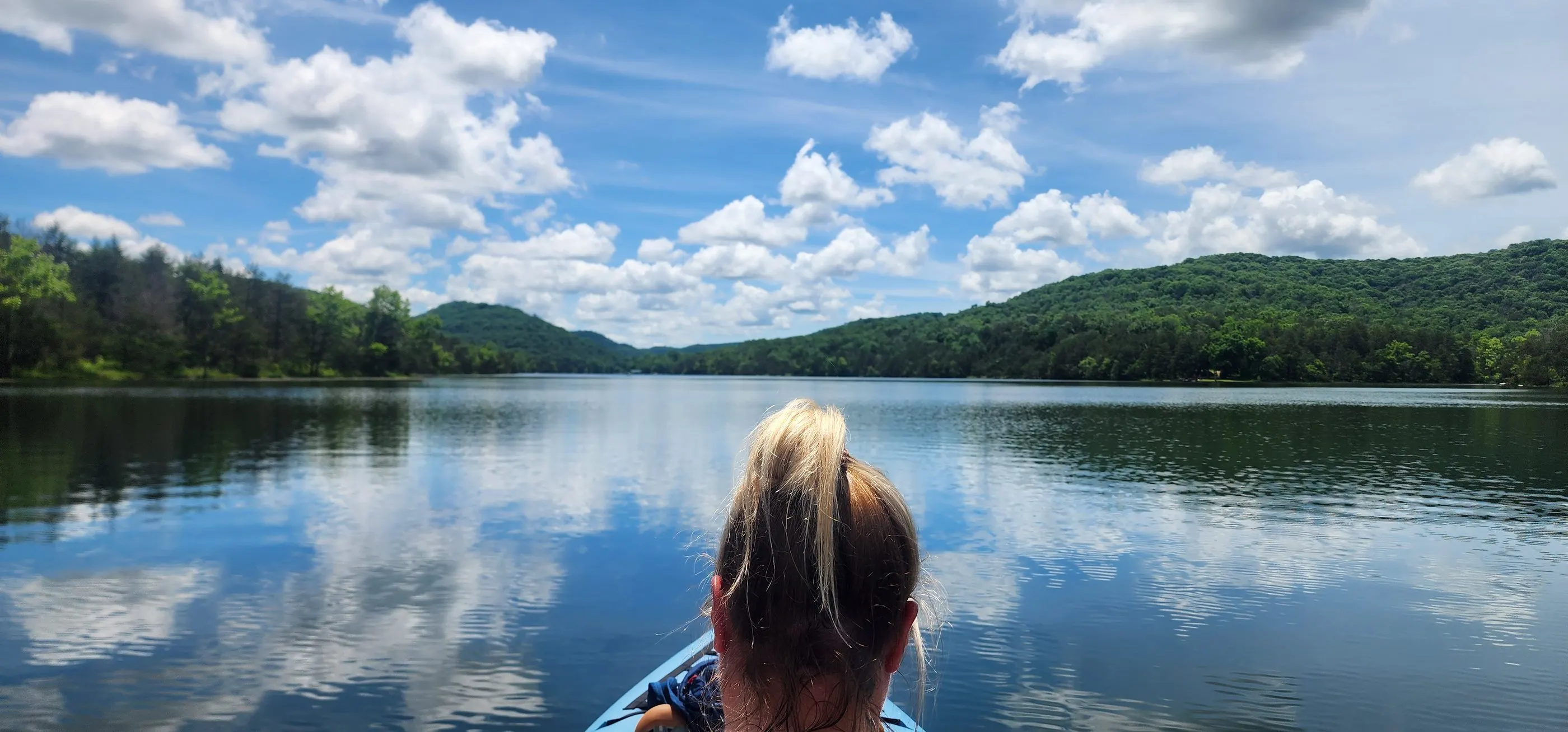 Brittany kayaking on a calm lake under a big blue sky with puffy clouds